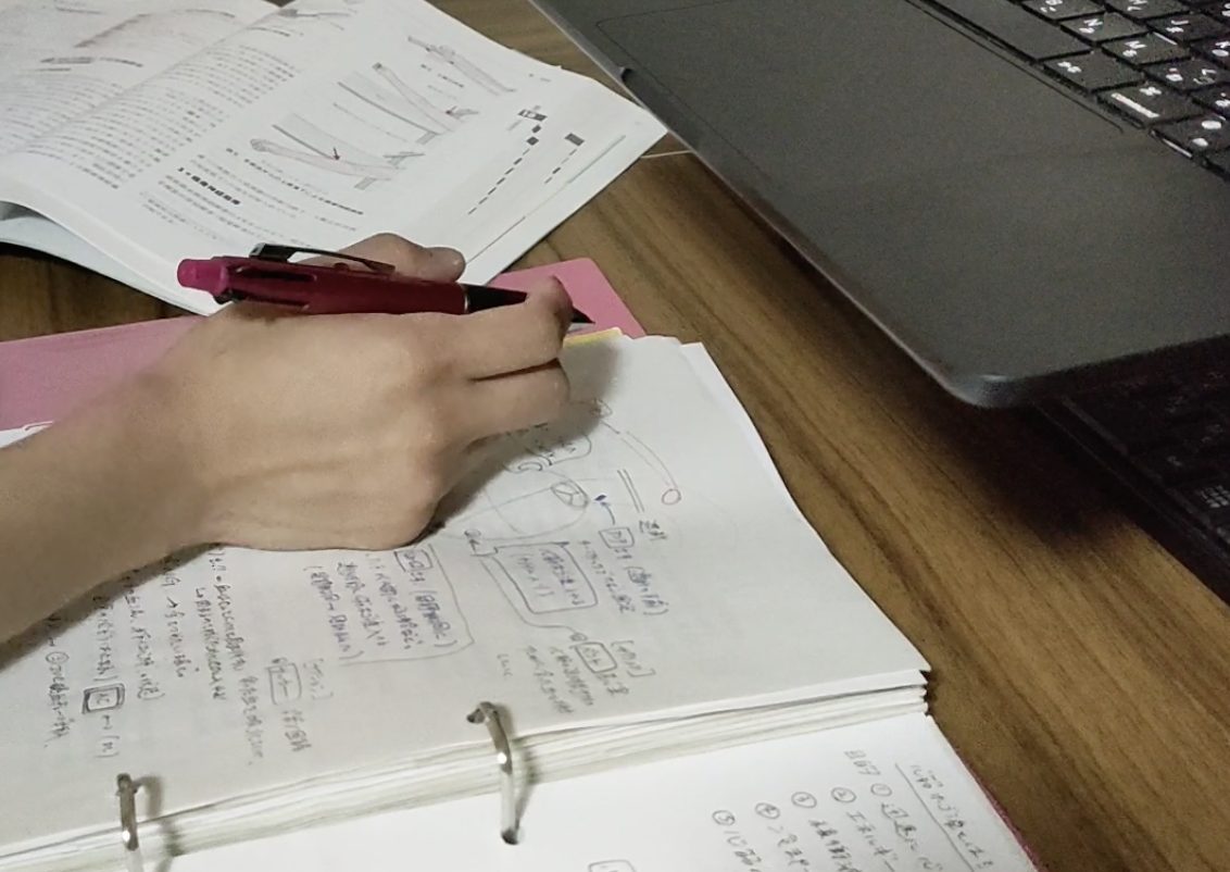 机に広げたノートに振り返りを書き込む手